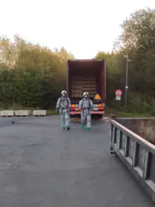 Zwei Einsatzkräfte in Chemikalienschutzanzügen vor geöffnetem Lkw mit Paletten und Sicherungsmulde im Industriegebiet Rehren
