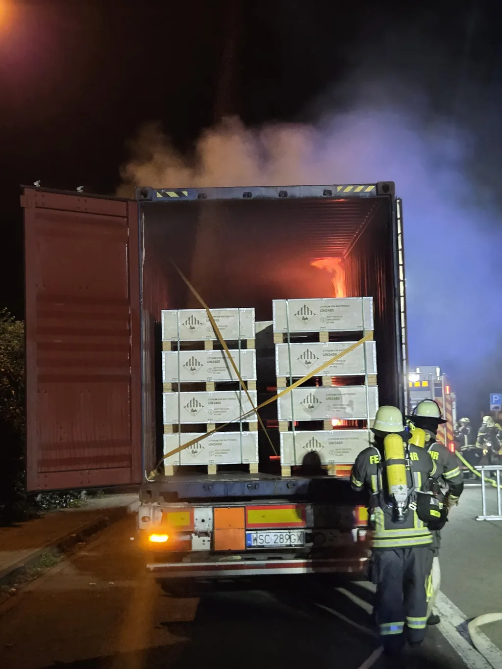 Feuerwehrkräfte unter Atemschutz am geöffneten Lkw-Container mit brennender Lithium-Ionen-Batterieladung auf dem Rastplatz Auetal Süd